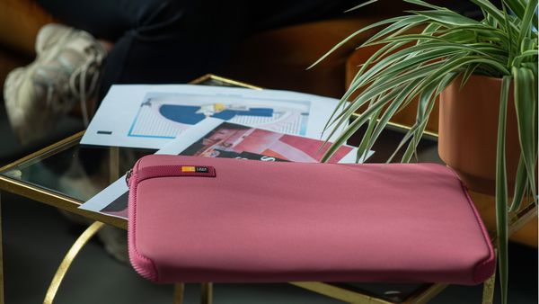 A pink Case Logic laptop sleeves sits on an end table next to some papers